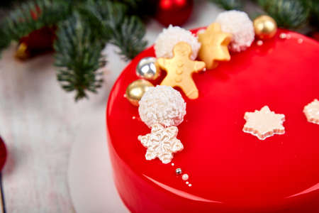 Mousse Christmas pastry cake dessert covered with red mirror glaze with new year decorations on garland lamps bokeh white background, Modern european cake Christmas theme.の写真素材
