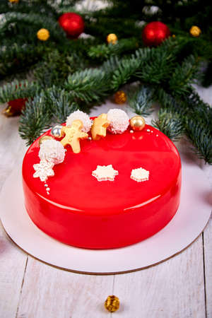 Mousse Christmas pastry cake dessert covered with red mirror glaze with new year decorations on garland lamps bokeh white background, Modern european cake Christmas theme.の写真素材