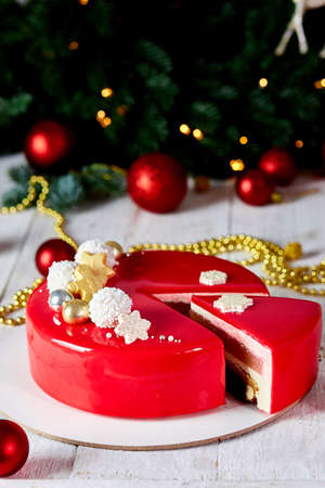 Mousse Christmas pastry cake dessert covered with red mirror glaze with new year decorations on garland lamps bokeh white background, Modern european cake Christmas theme.の写真素材