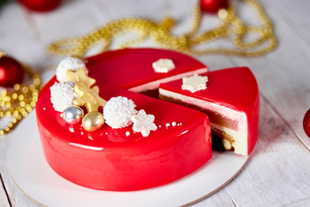 Mousse Christmas pastry cake dessert covered with red mirror glaze with new year decorations on garland lamps bokeh white background, Modern european cake Christmas theme.の写真素材
