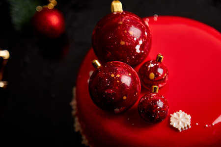 Mousse Christmas pastry cake dessert covered with red mirror glaze with new year decorations on garland lamps bokeh dark background, Modern european cake Christmas theme.の写真素材