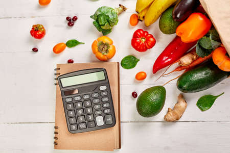 Flat lay paper shopping bag with assortment of fresh vegetables and fruits and calculator, bio healthy, organic food on white background, super market style, grocery, diet veggie food.の写真素材
