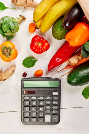 Flat lay paper shopping bag with assortment of fresh vegetables and fruits and calculator, bio healthy, organic food on white background, super market style, grocery, diet veggie food.の写真素材