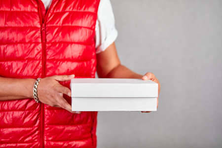 Delivery man employee in red vest uniform hold empty cardboard box isolated on grey background studio, Service quarantine pandemic, Contactless delivery.の写真素材
