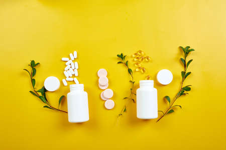 Flat lay of pills, fish oil, vitamins  with green leavws on yellow background, Healthcare concept,...