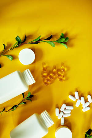 Flat lay of pills, fish oil, vitamins  with green leavws on yellow background, Healthcare concept, healthy food, supplements for healthy good life, Immune booster, hard light, trend.の写真素材