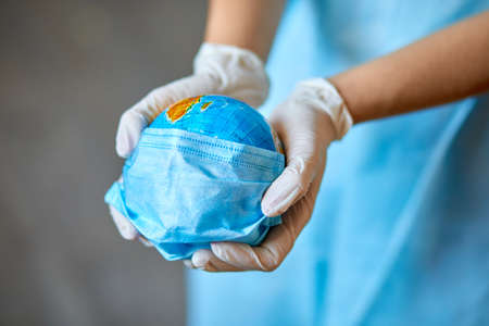 Globe in a medical mask in the hands of the doctor, Symbol that people all over planet are quarantined due to epidemic and pandemic of.の写真素材