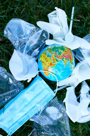 A globe in a pile of scattered garbage on a background of green grass, Around scattered plastic, protective mask, gloves, waste during pandemic. Save the World.の写真素材