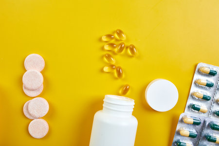 Flat lay of pills, fish oil, vitamins on yellow backgroundの写真素材