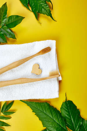 Bamboo toothbrushes and ear sticks, and green leaves on yellow paper background, Eco-friendly, Zero waste personal hygiene products, dental care conceptの写真素材