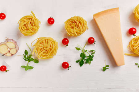 Ingredients for cooking pasta - tagliatelle, tomato, garlic, basil, parmesan cheese on white wooden background flat lay, top view, frame, copy space, Italian food concept.の写真素材