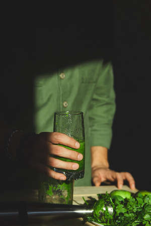 Man hold in hand glass with healthy detox smoothie, cooking with blender with fresh fruits and greens spinach at home, Lifestyle detox concept. Lifestyle detox concept. Vegan drinks.の写真素材