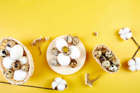 Easter flat lay composition  with cotton flowers and easter eggs in a small basket on yellow...
