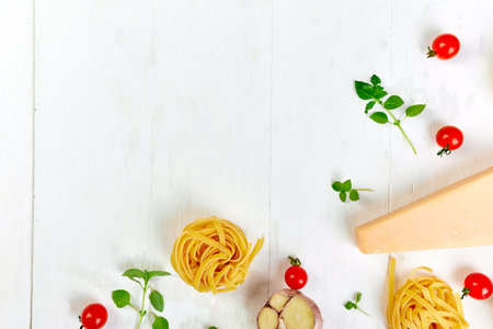 Ingredients for cooking pasta - tagliatelle, tomato, garlic, basil, parmesan cheese on white wooden background flat lay, top view, frame, copy space, Italian food concept.の写真素材