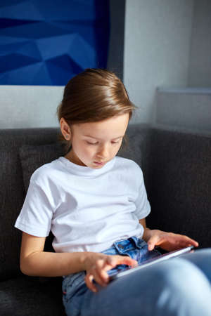 Cute little girl using a digital tablet, sitting on sofa, play game, and smiling, or child at home...
