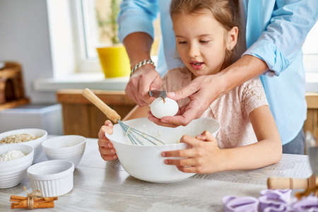 Father and daughter preparing dough together in kitchen, adding eggs to bowl while cooking pastry at home, Family cooking at home, fatherhood and family weekend concept.の写真素材
