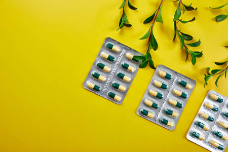 Flat lay Organic medical pills, capsules in blisters with green leaf, herbal plant on a yellow...