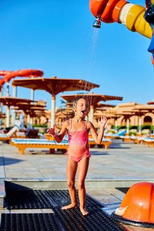 Funny little girl in swimsuit cooling in shower outside, child play with water in resort near swim pool, summer time, vacation.の写真素材