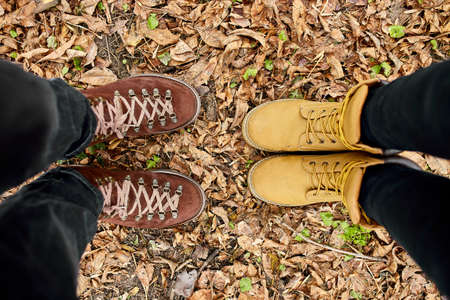 Modern young couple in hiking boots standing fallen autumn leaves in the forest, outdoor travel...