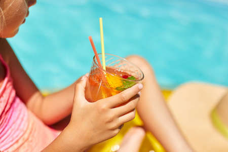 Little girl relaxing in swimming pool, enjoying suntans, drink a juice on inflatable yellow mattress...