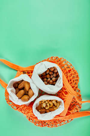 Top view of various sort of nuts on the table in a paper bag in shopping grocery bag on green background, Zero Waste Food Shopping. Waste-free living, nuts delivary. Copy space.の写真素材