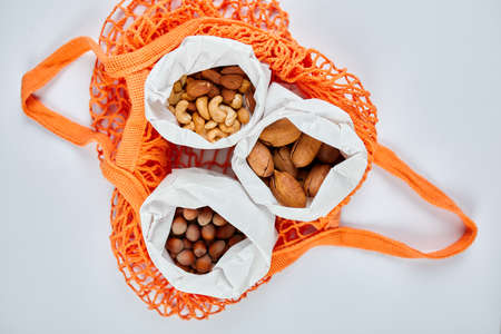 Top view of various sort of nuts on the table in a paper bag in shopping grocery bag on white background, Zero Waste Food Shopping. Waste-free living, nuts delivary. Copy space.の写真素材