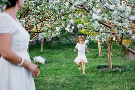 Happy woman and child, Cute daughter and mother in blossom spring garden, Wearing white dress outdoors, Spring season is coming. Mothers day holiday conceptの写真素材