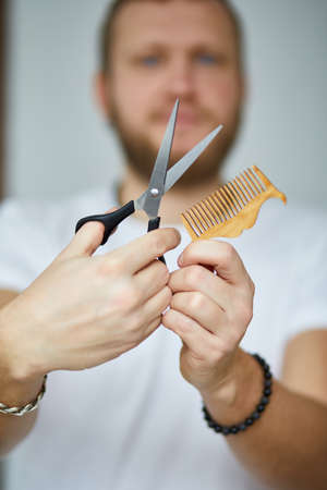 A male hairdresser wih bread holds scissors and a comb in his hands, barbershop, portrait of a trendy barber man shaving tools in his hands, copy space.の写真素材