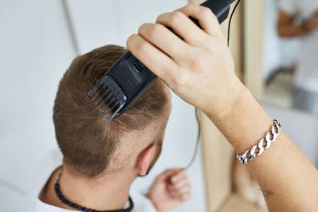 Handsome man in white t-shirts cutting hair personally himself with machine trimmer, clipper at...