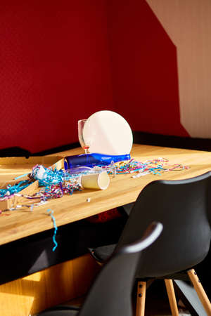 Messy wooden table with pizza box, empty blue bottles, wine glass and party decorations at morning after party celebration, After party chaos, Celebration leftovers.の写真素材