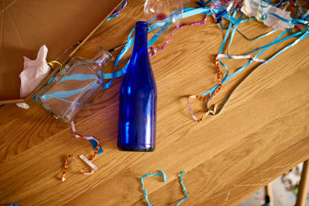 Messy wooden table with pizza box, empty blue bottles, wine glass and party decorations at morning after party celebration, After party chaos, Celebration leftovers.の写真素材