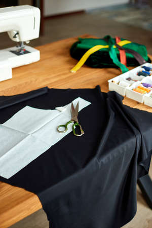 Sewing supplies and machine on a wooden table: sewing thread, scissors, pieces of cloth, needles, centimeter, pattern. Designer work place sewing machine in officeの写真素材