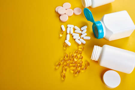 Flat lay of pills, fish oil, vitamins with green leavws on yellow background, Healthcare concept, healthy food, supplements for healthy good life, Immune booster.の写真素材