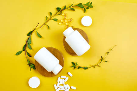 Flat lay of pills, fish oil, vitamins with green leavws on yellow background, Healthcare concept, healthy food, supplements for healthy good life, Immune booster.の写真素材