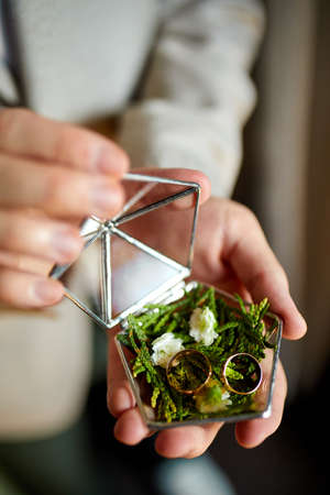 Groom men holding wedding rings lie on a beautiful, decorative hand made rustic box with plants...