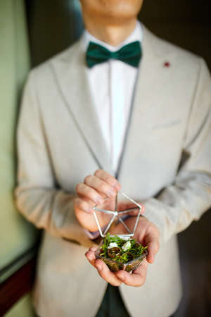 Groom men holding wedding rings lie on a beautiful, decorative hand made rustic box with plants inside, copy space,  Tears of happiness, symbol of love. Wedding dayの写真素材
