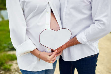 Unrecognizable couple, future parents, pregnant young woman and a man touching belly, waiting for a miracle, Pregnant tummy close up, outdoor in spring or summer parkの写真素材
