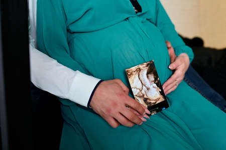 Unrecognizable pregnant couple holding ultrasound scan , future parents, waiting for a miracle, Pregnant tummy close up, outdoor in spring or summer parkの写真素材