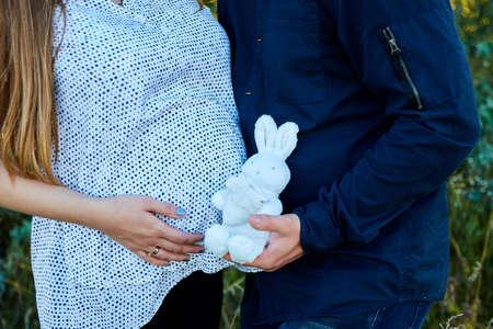 Unrecognizable couple, future parents, pregnant young woman and a man touching belly, waiting for a miracle, Pregnant tummy close up, outdoor in spring or summer parkの写真素材