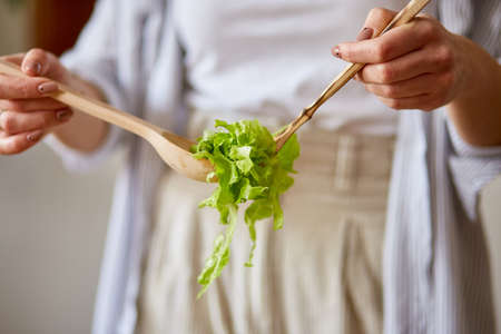 Woman is preparing vegetable salad in the kitchen, mixing leaf of salad and vegetables ina white bowl, Healthy food concept, vegan or diet.の写真素材