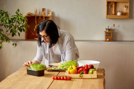 Woman is cooking in the kitchen at home, using digital tablet or smarthone, looking recipe, Healthy...