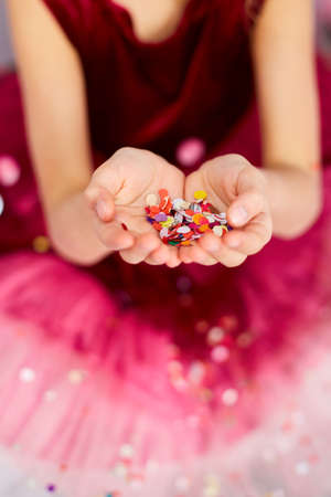 Beautiful little girl blows up multicolored confetti, having fun at home birthday party. Happy...