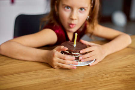A greedy little girl is wearing a birthday hat hold at a Birthday Cake, make faces, for a celebration party concept.の写真素材