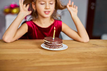 A little girl is wearing a birthday hat makes a wish , looking at a Birthday Cake, with glowing candles for a celebration party concept.の写真素材