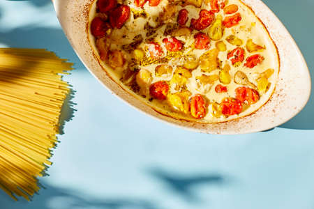 Trending viral recipe of baked tomatoes and feta with pasta, Fetapasta on a blue background sunlight, hardlight . New, popular dinner dish, Top view, copy space.の写真素材