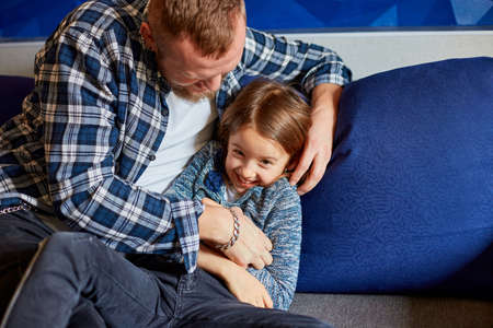 Smiling father with daughter having fun, tickle at sofa in living room, at home. Happy family.