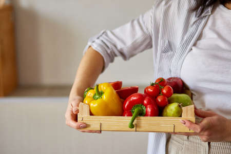Woman holding wooden box with natural fresh vegetables and fruits  for cooking. Bio organic food, healthy eating, Shopping, grocery store.  Diet and vegetarian concept.の写真素材