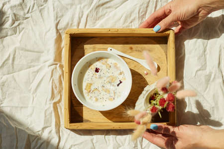 Woman in jeans sitting on the bed, and eating healthy granola bowl during the morning sunlight, breakfast in the bed.の写真素材