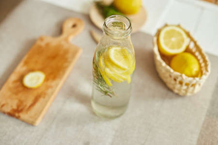 Glass bottle  detox healthy water with lemon and rosemary, fresh lemonade in glass on a white table...
