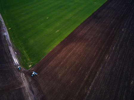 Aerial view of a modern green tractor plowing dry agricultural field , preparing land for sowing,...